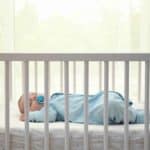 baby sleeping in a blue sleep sack in a crib during daytime