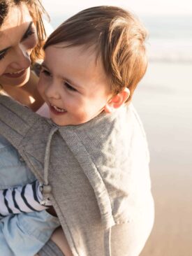 Mom carrying young baby on the beach in an organic baby carrier