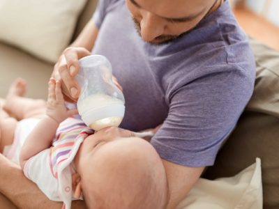 man bottle feeding baby with goat milk formula