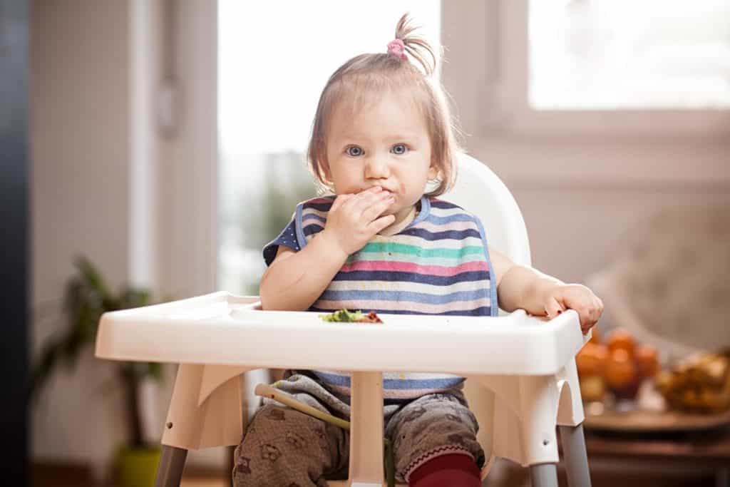 baby feeding herself in high chair