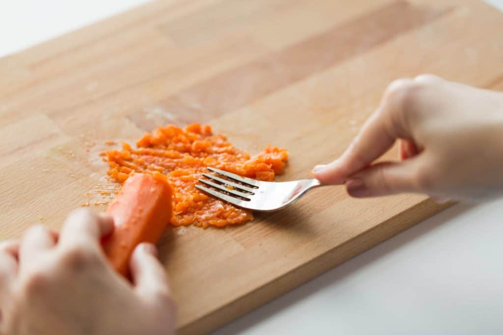 person mashing a steamed carrot 