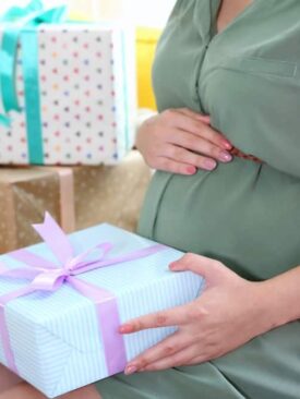 pregnant woman holding an unwrapped gift with several wrapped gift boxes next to her