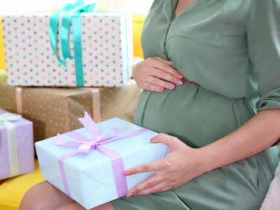 pregnant woman holding an unwrapped gift with several wrapped gift boxes next to her