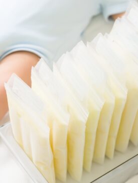 baby lying next to container holding frozen breast milk in bags