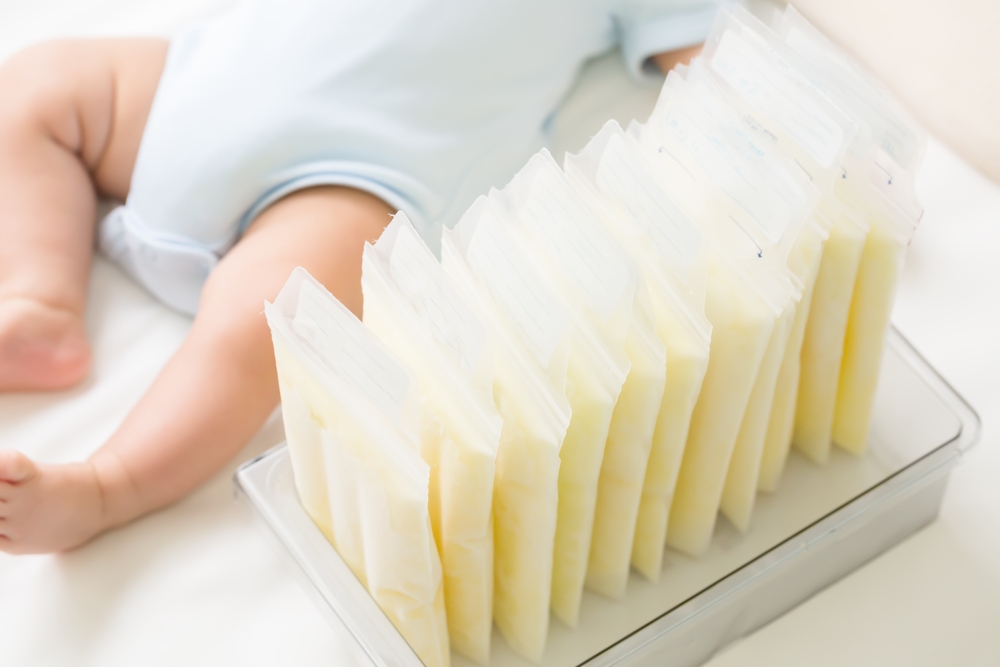 baby lying next to container holding frozen breast milk in bags