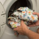 closeup of hands putting cloth diapers into front-loading washing machine to wash without harsh chemicals