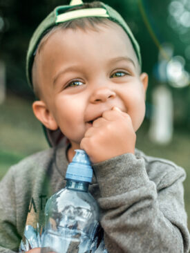 young toddler playing outside holding water bottle and smiling