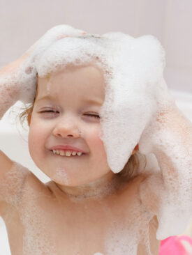 young toddler in bath with shampoo suds on her head