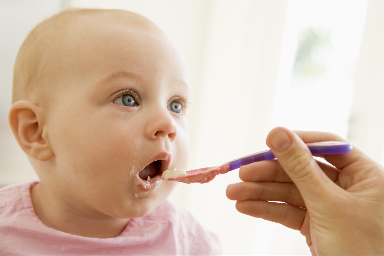 closeup of parent's hand spoon feeding baby