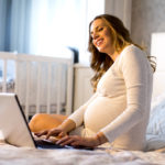 pregnant mom in baby's nursery looking at computer for virtual baby shower