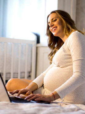 pregnant mom in baby's nursery looking at computer for virtual baby shower